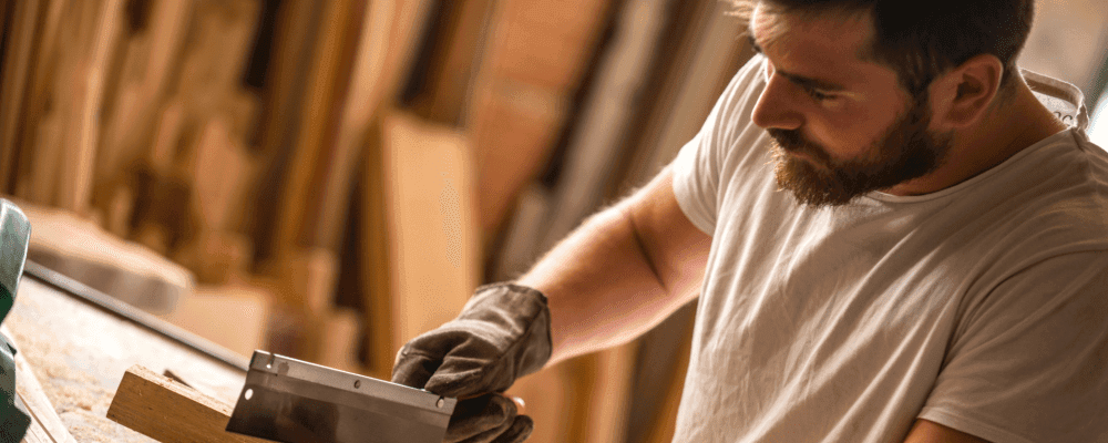 Dieses Bild zeigt eine Person, die eine Ausbildung zum/r Tischler/in absolviert. Die Person ist damit beschäftigt, Möbelstücke zu bearbeiten und herzustellen. Dabei verwendet sie verschiedene Werkzeuge, um das Holz zu bearbeiten und in die gewünschte Form zu bringen.