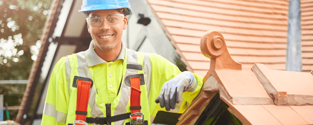 Auf diesem Bild ist eine Person zu sehen, die eine Ausbildung zum/r Dachdecker/in absolviert. Die Person ist damit beschäftigt, das Dach eines Hauses zu reparieren.