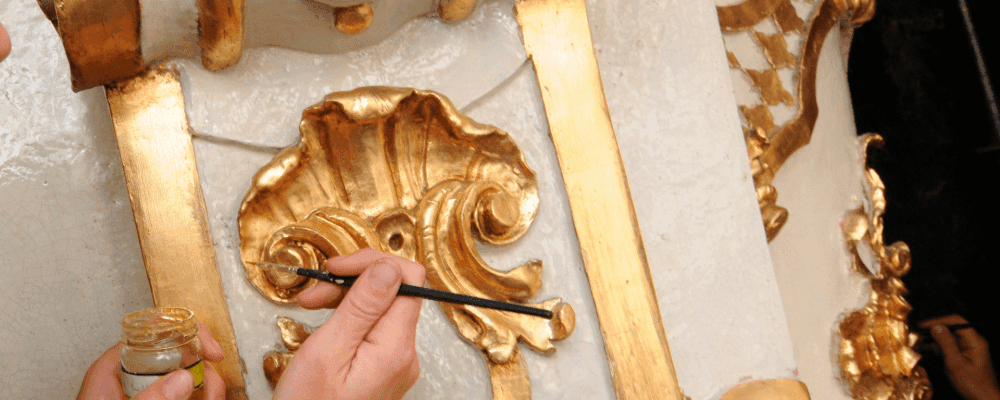 Auf diesem Bild ist eine Person zu sehen, die eine Ausbildung zum/r Vergolder/in absolviert. Die Person verwendet verschiedene Werkzeuge und Techniken, um Metalloberflächen mit Blattgold zu verzieren. Dieser Beruf erfordert viel Geschick und Präzision, um schöne Ergebnisse zu erzielen.