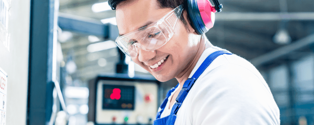 Auf diesem Bild ist eine Person zu sehen, die eine Ausbildung zum/r Zerspanungsmechaniker/in absolviert. Dieser Beruf umfasst die Herstellung und Bearbeitung von Metall- und Kunststoffteilen mittels computergesteuerter Maschinen. Die Person auf dem Bild ist damit beschäftigt, ein Metallteil zu bearbeiten.