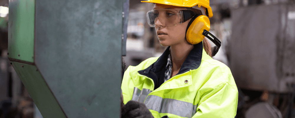 Auf diesem Bild ist eine Person zu sehen, die eine Ausbildung zum/r Fertigungsmechaniker/in absolviert. Dieser Beruf umfasst die Herstellung und Montage von Metall- und Kunststoffteilen. Die Person auf dem Bild ist damit beschäftigt, Teile für ein Gerät zu fertigen.