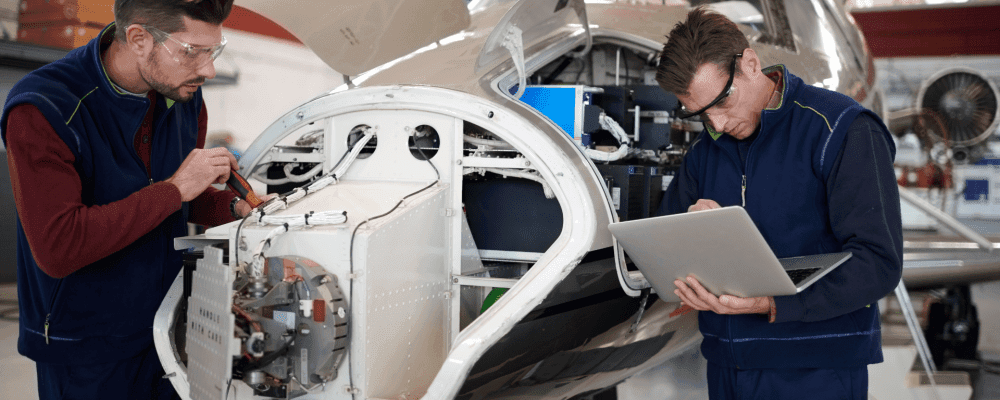 Auf diesem Bild ist eine Person zu sehen, die eine Ausbildung zum/r Fluggerätelektroniker/in absolviert. Dieser Beruf umfasst die Wartung und Reparatur von elektronischen Systemen in Flugzeugen. Die Person auf dem Bild ist damit beschäftigt, ein solches System zu warten und zu reparieren.