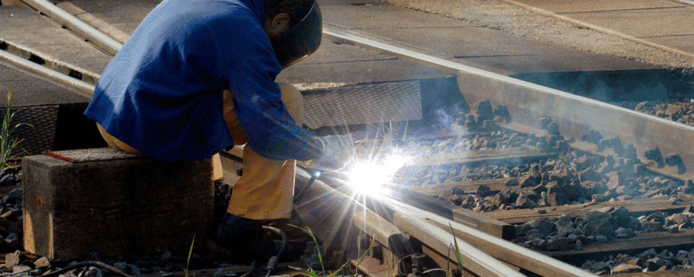 Auf diesem Bild ist eine Person zu sehen, die eine Ausbildung zum/r Gleisbauer/in absolviert. Gleisbauer sind für die Planung, Herstellung und Instandhaltung von Schieneninfrastrukturen verantwortlich. Sie arbeiten sowohl im Tief- als auch im Oberbau und übernehmen Aufgaben in der Bahnhofs- und Signaltechnik.